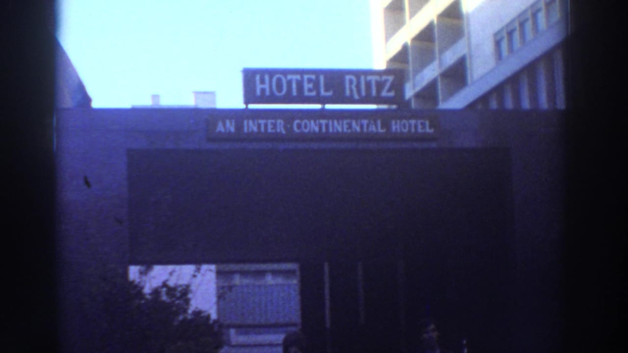 Hotel Ritz sign above a dark hotel entrance with bright sky and partial street-level figures.