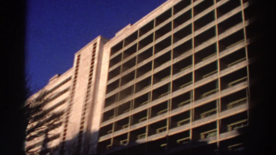 1976 Greece 8mm frame showing the hotel balcony grid from below, with strong sunlight, shadowed edges, and deep blue sky.