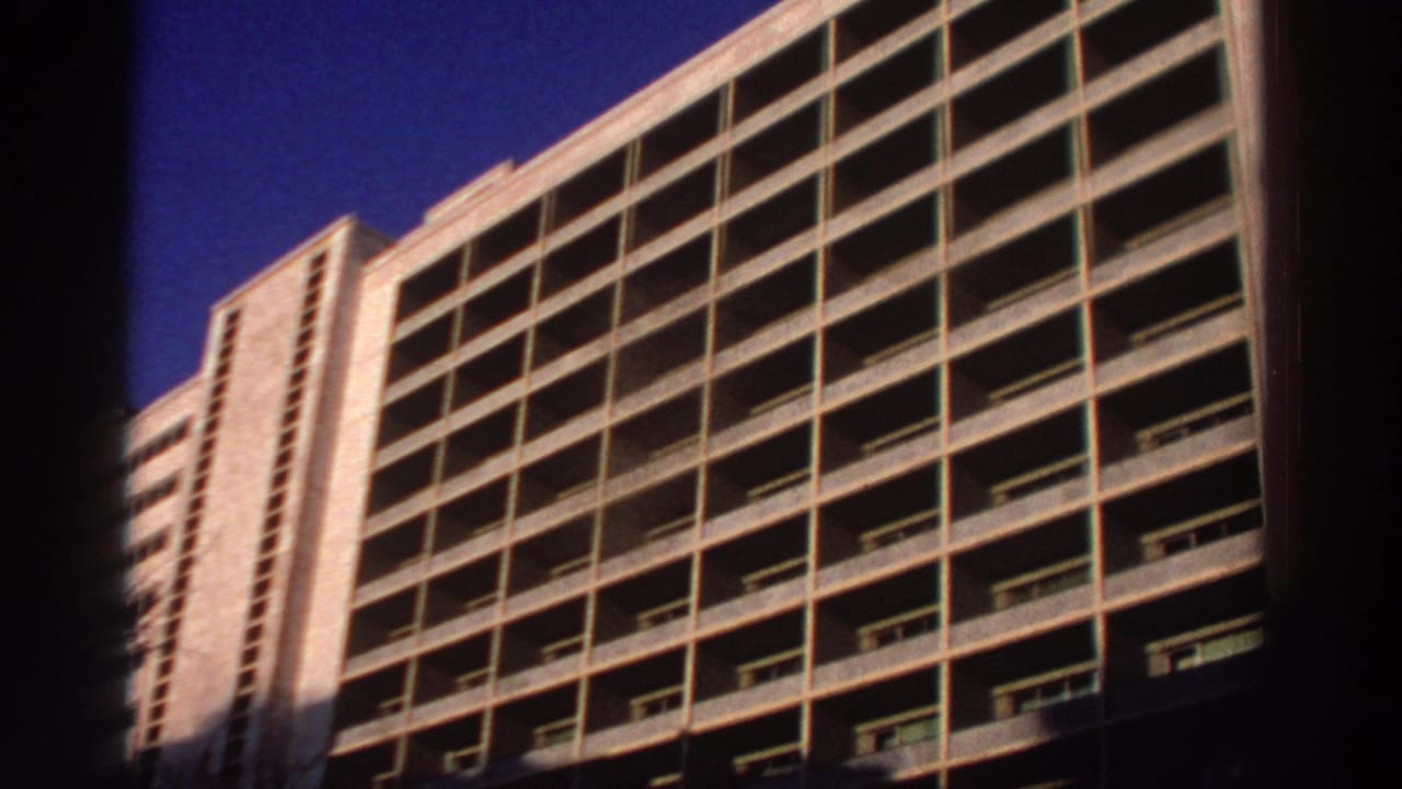 Low-angle view of a concrete hotel facade with gridded balconies under blue sky.