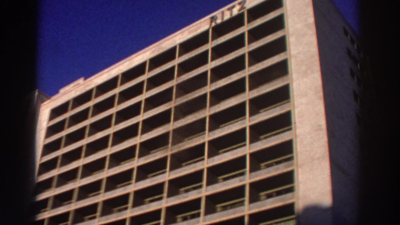 Concrete hotel facade with rooftop RITZ sign and rows of balcony openings.