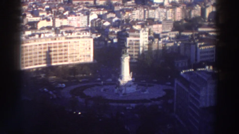 1976 Greece 8mm frame showing an elevated view across city blocks toward a roundabout with a central monument and surrounding buildings.
