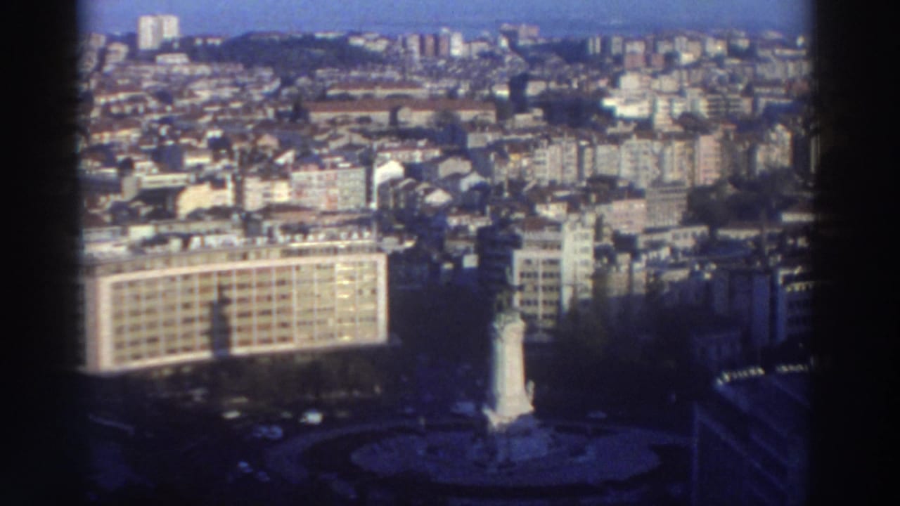 City skyline seen from above with a roundabout monument near the lower center and urban blocks beyond.