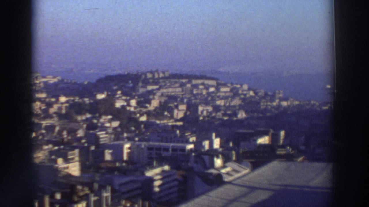 Hillside city panorama with bright buildings, coastline, water, and film border.