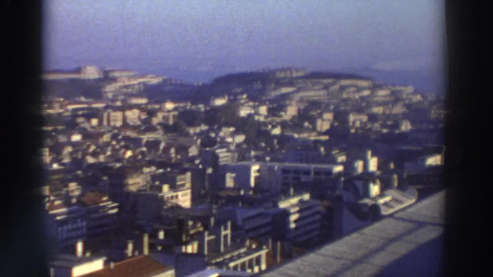 1976 Greece 8mm view over urban rooftops toward hillside buildings and a hazy coastal horizon.
