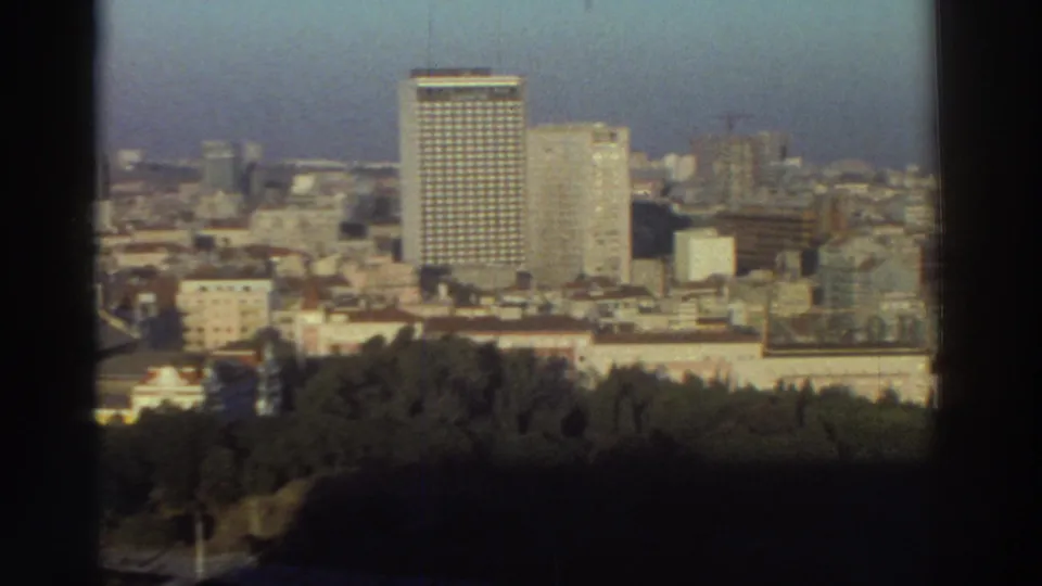 1976 Greek urban panorama from above, showing clustered high-rises and low buildings behind a dark foreground edge and trees.