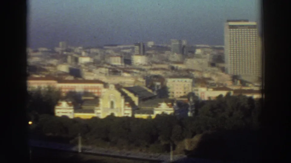 Elevated 1976 Greece city view with a pale yellow church facade near trees and a tall modern building on the right.
