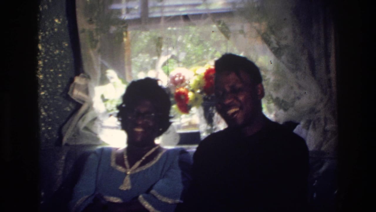 A woman in a blue dress and a man in a dark shirt sit smiling indoors.