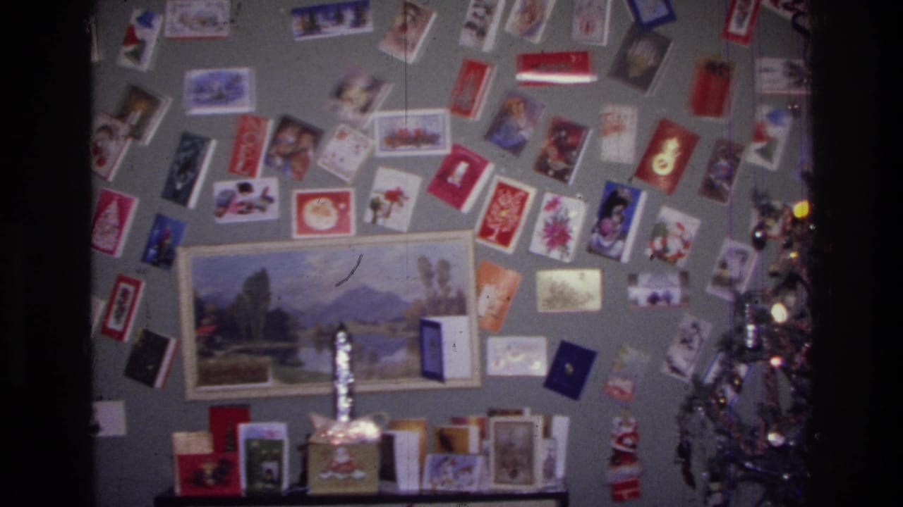 1976 Harlem interior with Christmas cards arranged across the wall, a landscape picture below, and a small lit tree at the right edge.
