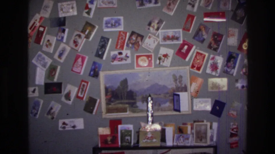 1976 Harlem living room detail showing many Christmas cards on a gray wall, a framed landscape print, and tabletop holiday items.
