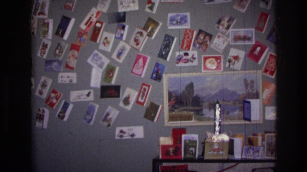 Wall covered with Christmas cards, postcards, a framed landscape print, and shelf items.