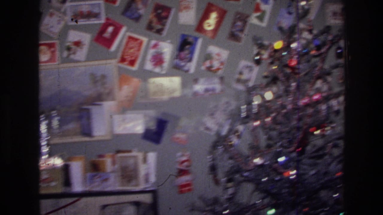 1976 Harlem home-movie frame showing a silver Christmas tree near a gray wall filled with holiday greeting cards.