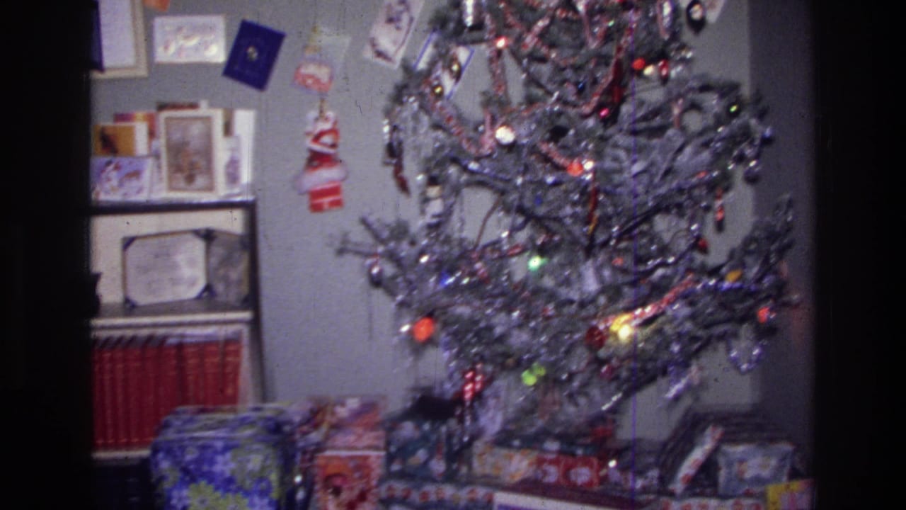 1976 Harlem home-movie frame showing a silver tinsel Christmas tree, ornaments, lights, and wrapped gifts in a private living room.