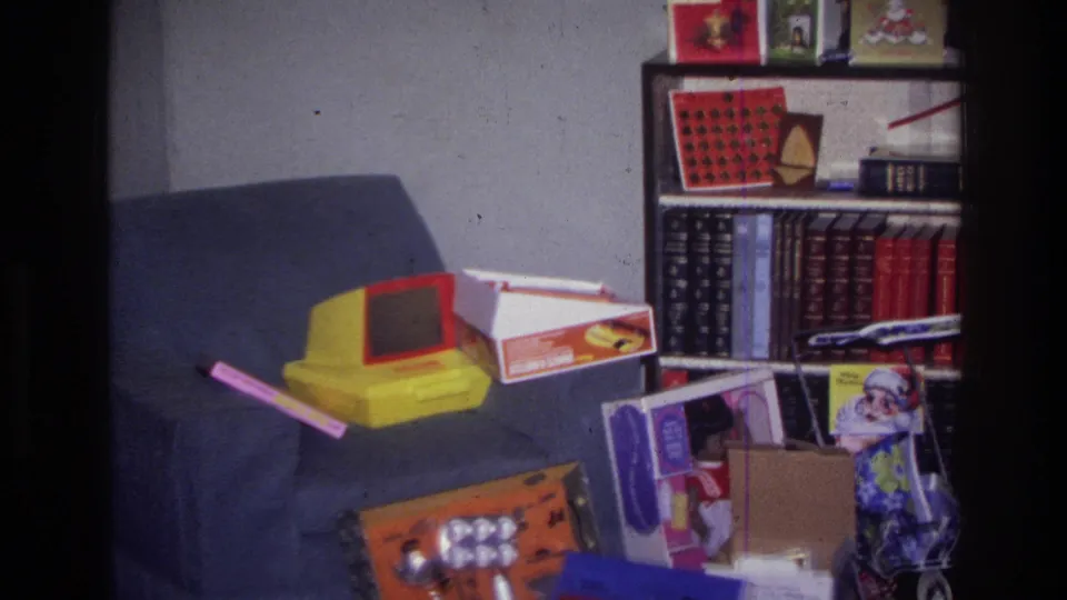 1976 Harlem Christmas interior showing a yellow tabletop toy, boxed presents, and toy packaging arranged near a couch and bookshelf.