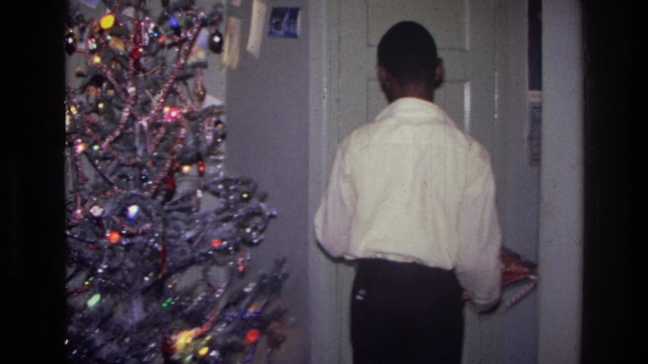 1976 Harlem home-movie frame of a person seen from behind beside a lit Christmas tree and holiday cards.