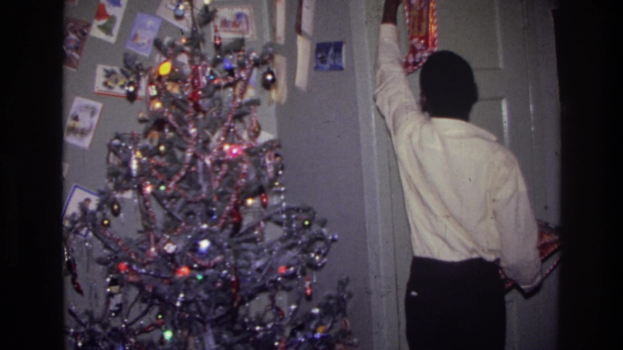 Person reaches toward a door frame near a Christmas tree covered with tinsel and ornaments.
