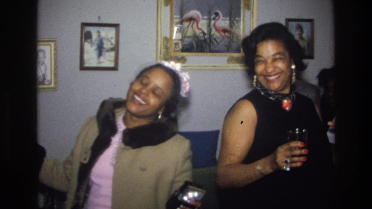 Women laugh and dance near framed wall art, with one woman holding a drink.