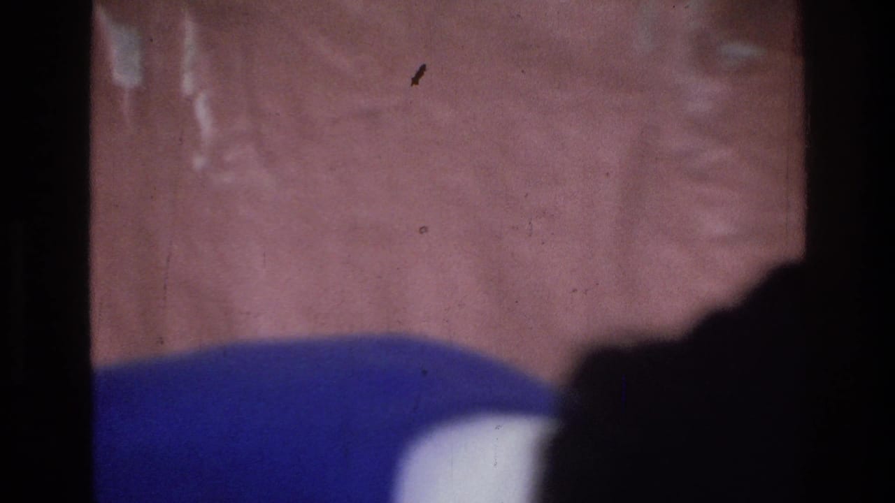 Blurred close view of a blue sweater and another person near a pink tablecloth.