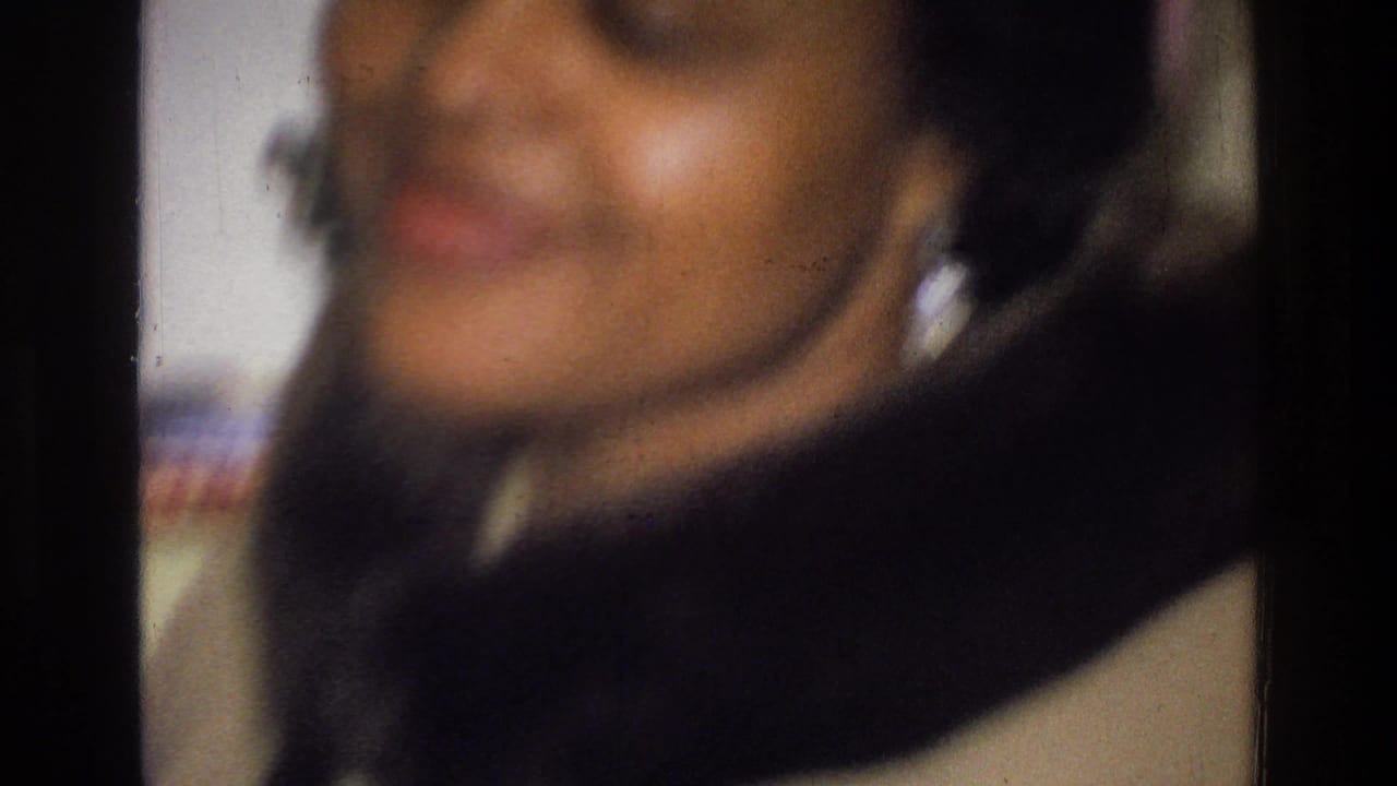 Close, blurred view of a smiling woman near the camera in an interior space.