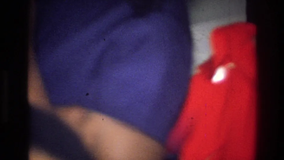 Blurred 8mm interior frame from the Harlem clip, showing a dark or purple garment and a bright red object close to the camera.