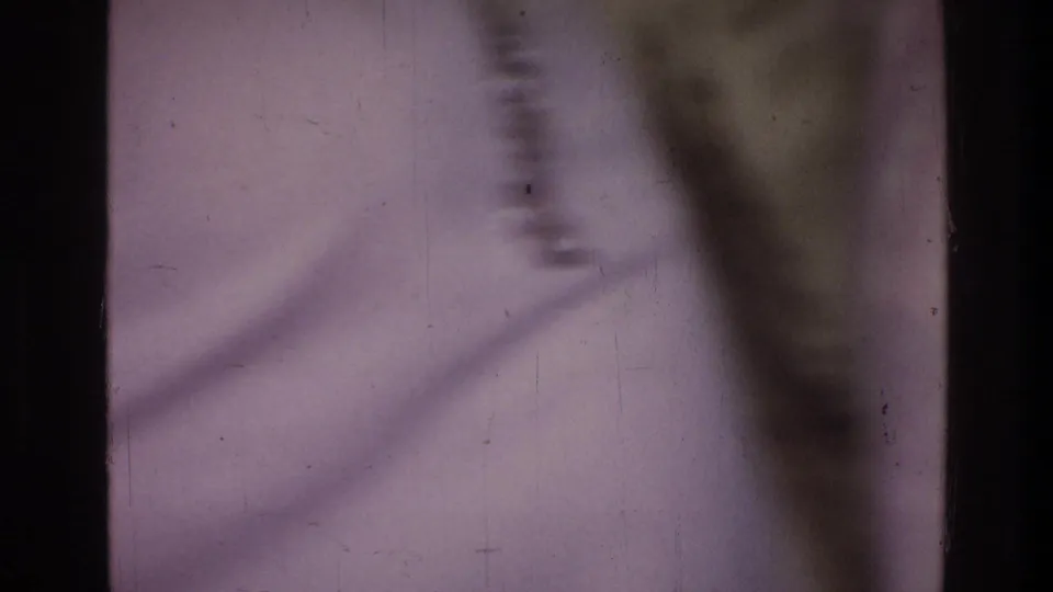 Soft-focus final 8mm frame from the 1976 Harlem interior, showing a pale surface, shadow, scratches, and analog film texture.