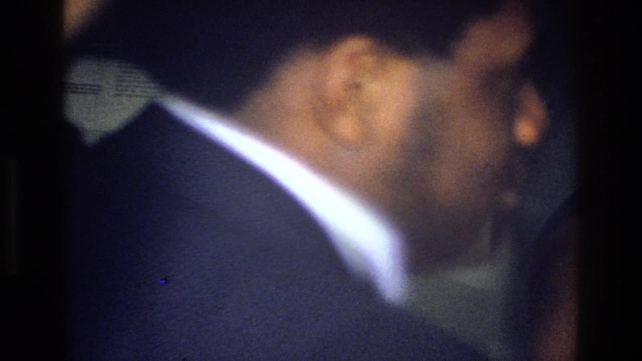 Soft-focus 1976 Harlem home-movie frame showing a person in dark clothing close to the camera inside a dim interior.