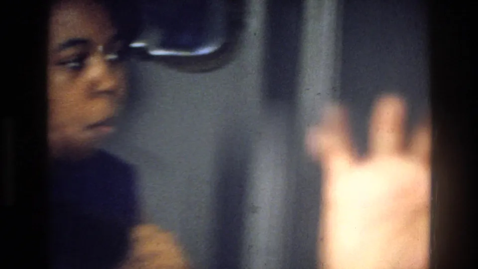 1976 Harlem home-movie frame showing a partially visible person near an interior door, with a raised hand close to the lens.