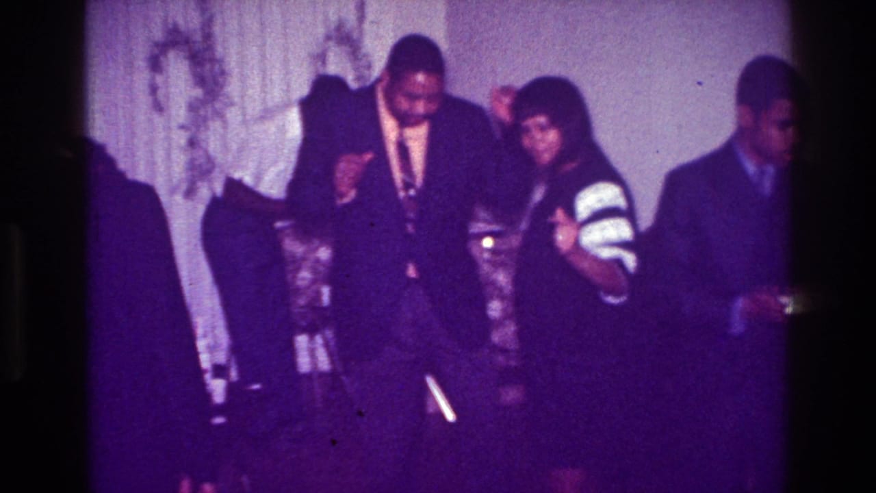 1976 Harlem party scene with adults dancing in formal attire inside a private room with curtains and soft purple film color.