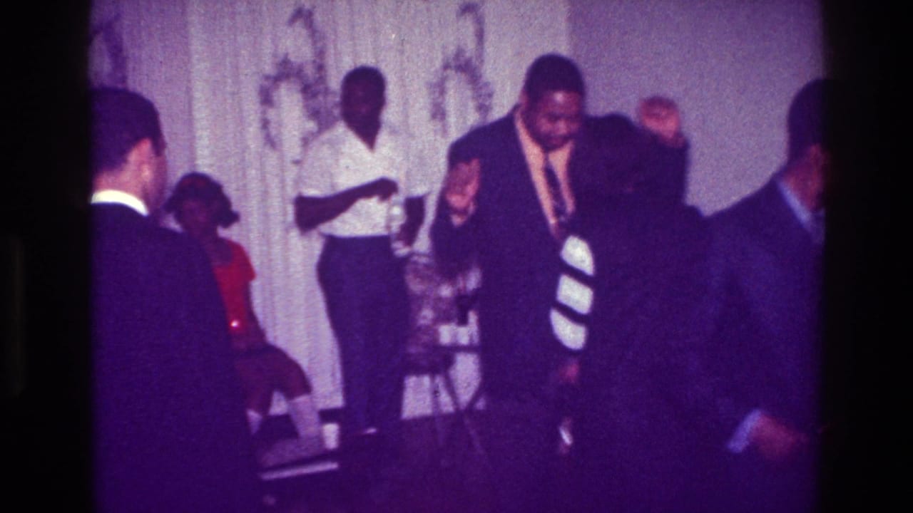 1976 Harlem party scene with a man in a dark suit dancing, a woman in a striped dress nearby, and a bottle held behind them.