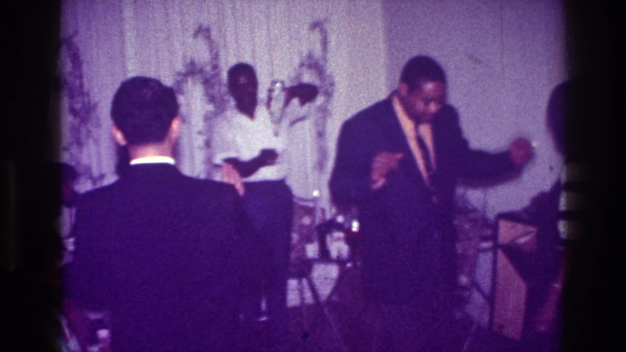 Dancing man raises his arms near a man in a white shirt.