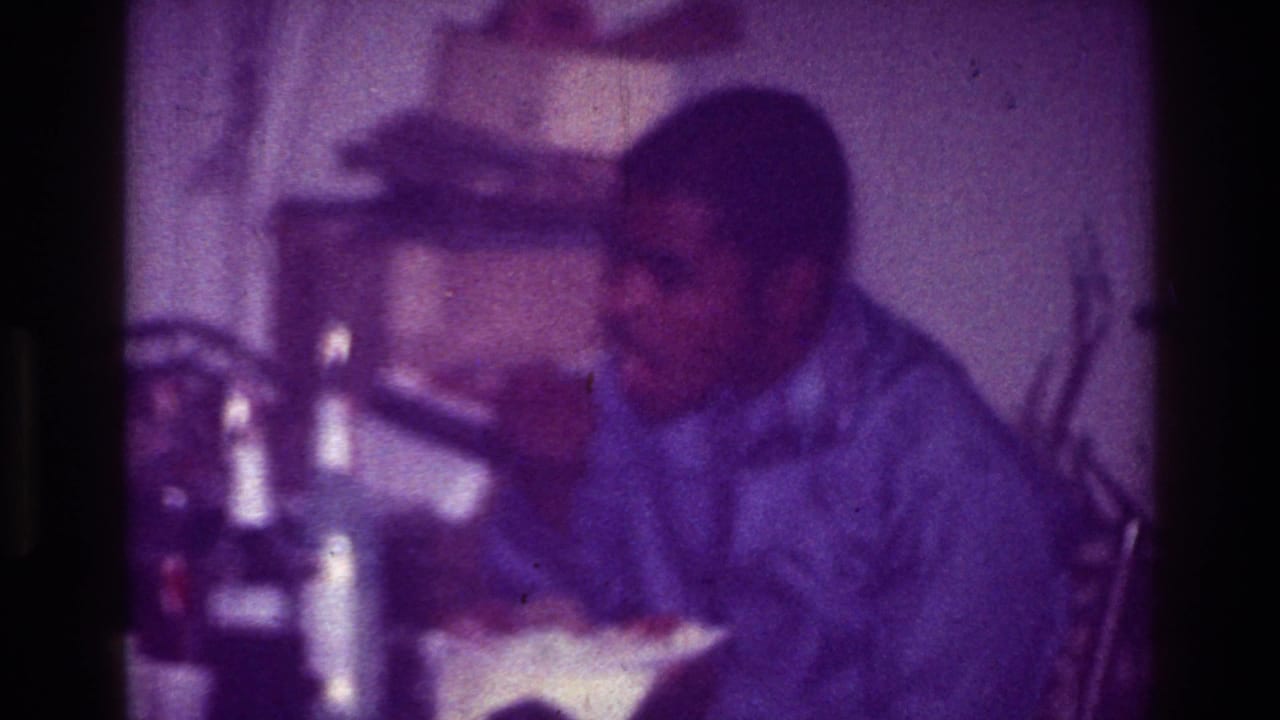 In 1976 Harlem home-movie footage, a seated Black man eats from a bowl in a soft, grainy interior.