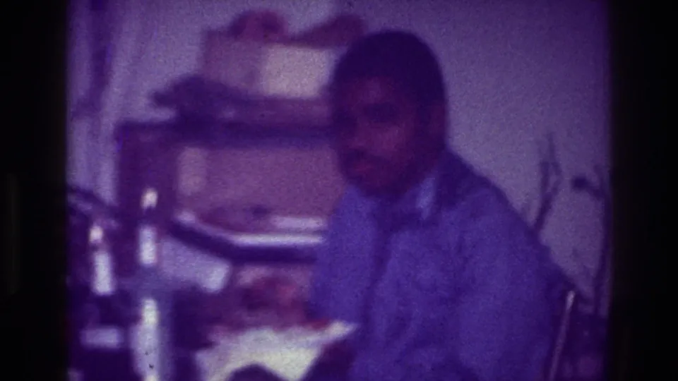 At the end of the clip, the seated man is still at the table in a grainy 1976 Harlem home interior.