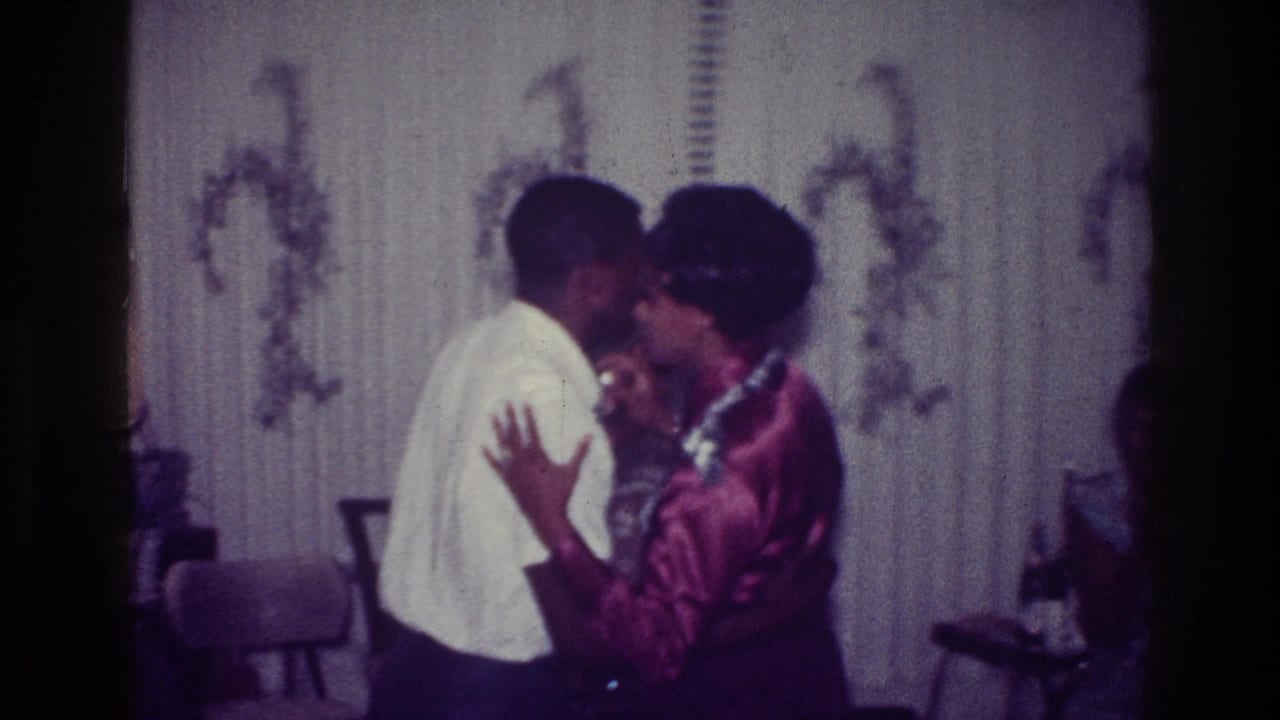 Couple dancing closely and kissing in front of patterned curtains.