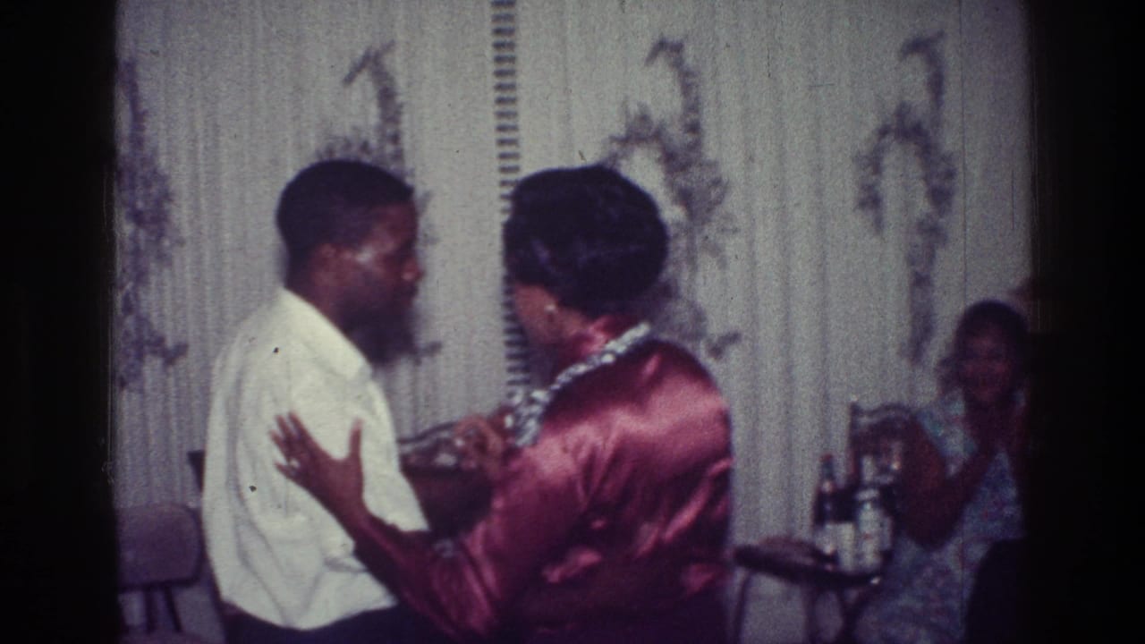 In 1976 Harlem home-movie footage, a Black couple dances closely in a private room while another person sits near a small table behind them.