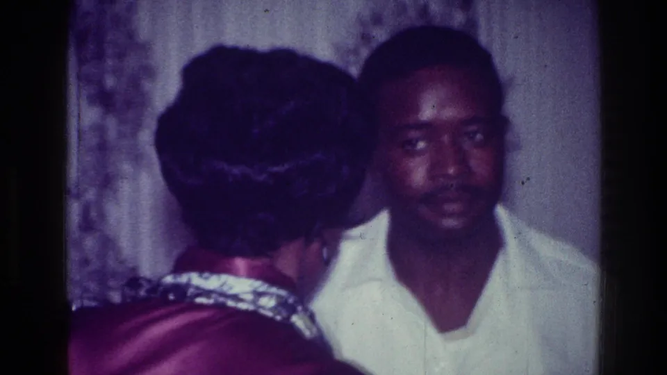 The handheld 8mm frame moves closer as the couple dances, showing the woman’s updo and patterned collar beside the man’s face.