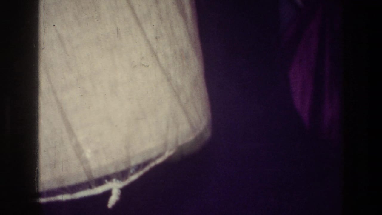 1976 Harlem home-movie frame showing a dim room corner with a lampshade and a partially visible person in shadow.