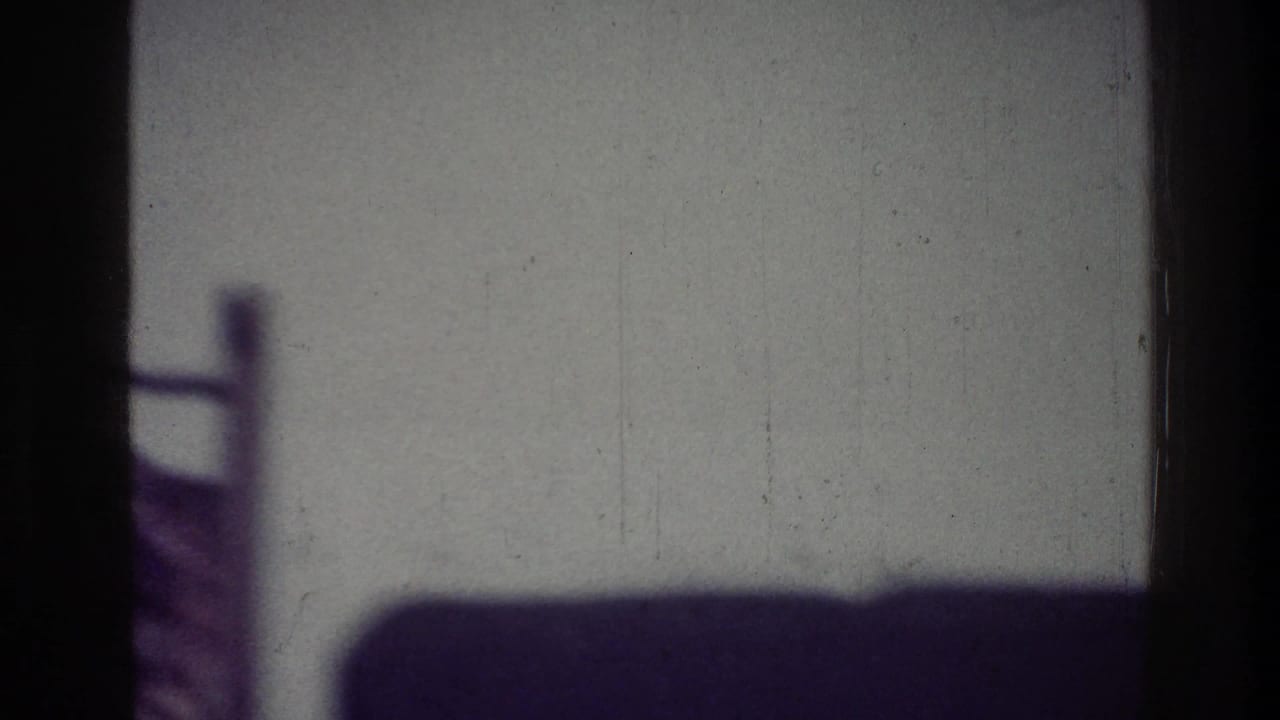 1976 Harlem home-movie frame with a pale backlit surface, dark side borders, and a soft shadow shape near the bottom.