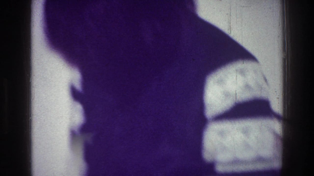 1976 Harlem frame showing a shadowy human silhouette near a bright window or wall, obscured by purple cast and low light.