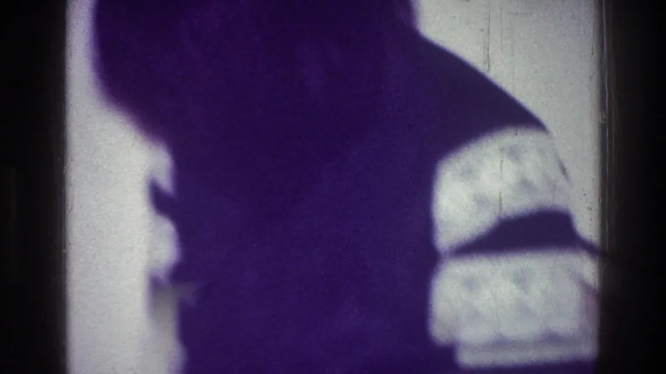 1976 Harlem frame showing a shadowy human silhouette near a bright window or wall, obscured by purple cast and low light.