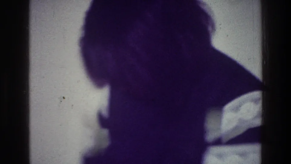 1976 Harlem home-movie frame with an indistinct person in dark silhouette against a pale backlit surface and visible film scratches.