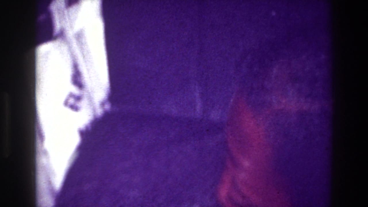 Partial close-up of a person beside a bright white garment or object in a dim interior.