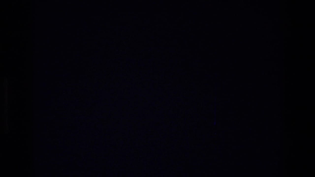 Dim 8mm frame from the indoor Harlem sequence, with most of the image falling into darkness between visible moments.