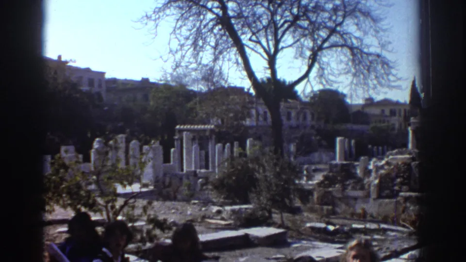 Tel Aviv home-movie frame showing sunlit stone ruins or historic structures, bare trees, and partial figures at the bottom edge.