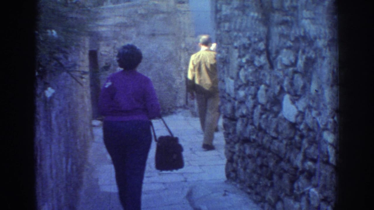 1976 Tel Aviv frame of a woman in a purple sweater and a man walking away through a narrow stone passage.