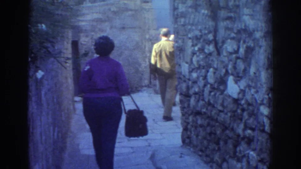 1976 Tel Aviv frame of a woman in a purple sweater and a man walking away through a narrow stone passage.