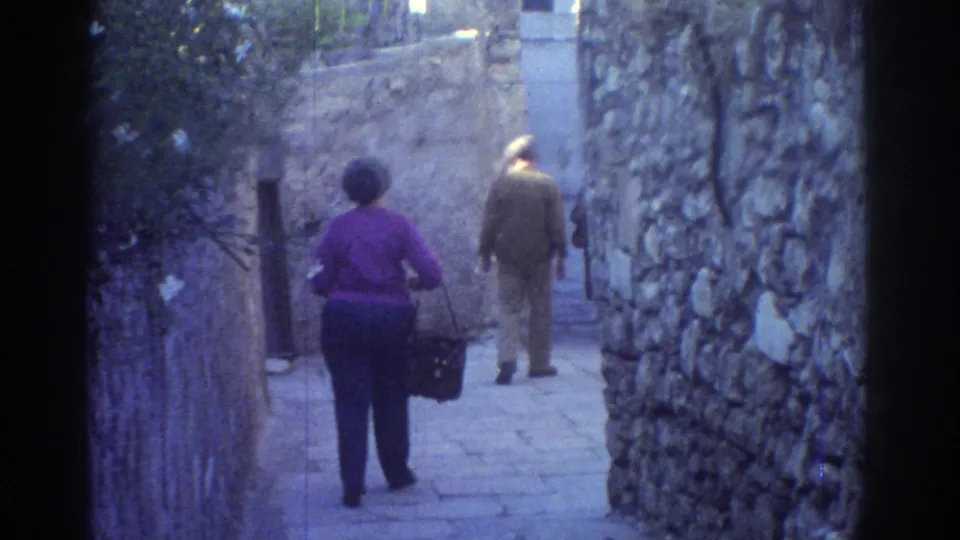 1976 Tel Aviv frame showing a woman with a handbag and a man walking farther down a stone-lined alley.