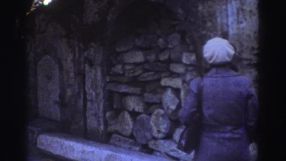 1976 Tel Aviv home-movie frame showing a woman from behind as she looks toward rough stone masonry and arched ruins.