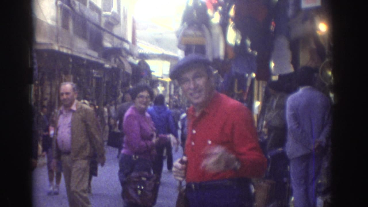 Man in a red shirt and blue cap faces the camera in a crowded market street.