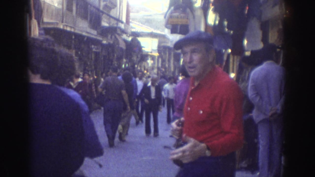Man in red stands near the right edge as shoppers walk down the market lane.