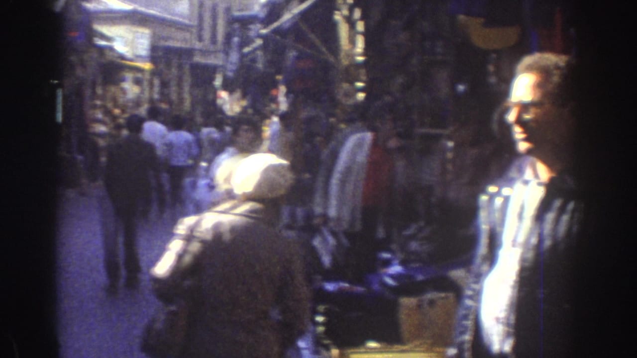 Crowded narrow market street with pedestrians and shopfronts on both sides.