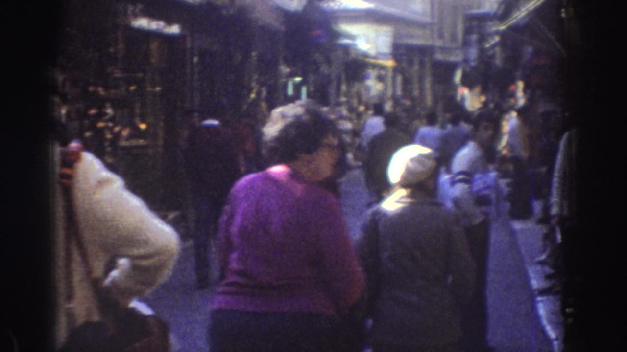 Pedestrians pass through a crowded market lane beside shop displays.